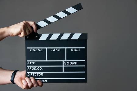96626099-a-movie-production-clapper-board-hands-with-a-movie-clapperboard-on-grey-background-with-copy-space-